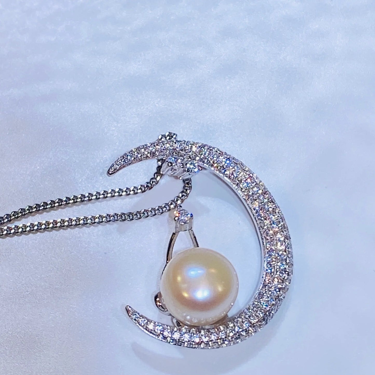 This unique moon-shaped necklace is meticulously handcrafted from sterling silver and set with hundreds of micro-zircon stones for a stunning, sparkling effect. A natural freshwater pearl rests elegantly on the moon's curve, adding a touch of classic sophistication to this modern design. The piece is finished with a luxurious 18K gold plating, making it a versatile and captivating addition to any collection.