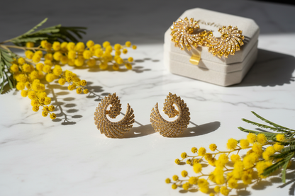 Gold pinwheel spiral pavé CZ stud earrings on marble surface with yellow flowers, lifestyle jewelry photography